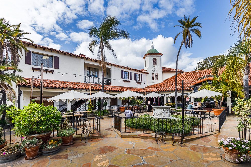 A lovely courtyard ijn downtown Santa Barbara, with flgstone pavers, fenced greenery, tables and chairs, and a bell tower.